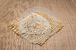 Oat cereal grain. Grains on square cutout of jute. Wooden table.