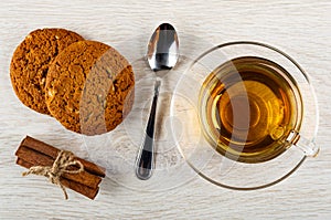 Oat cookies with sunflower seeds, cinnamon sticks, spoon, cup of tea in saucer on wooden table. Top view