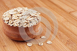 Oat-flake in wooden bowl on brown bamboo board, closeup. Healthy dietary cereals background.