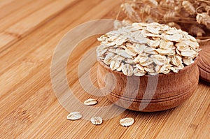 Oat-flake in wooden bowl on brown bamboo board, closeup. Rustic style, healthy dietary cereals background.