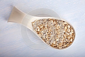 Oat flakes in big porcelain spoon on white background,