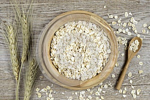 Oat flakes in bowl ,wooden spoon and and golden wheat ears.on wooden background.