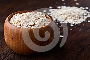 Oat flakes in bowl and wooden spoon isolated on wooden background, close-up, top view, selective focus.