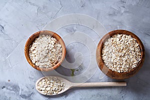 Oat flakes in bowl and wooden spoon isolated on wooden background, close-up, top view, selective focus.