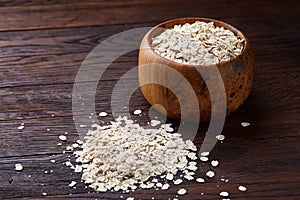 Oat flakes in bowl and wooden spoon isolated on wooden background, close-up, top view, selective focus.