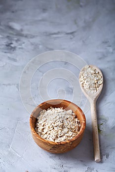 Oat flakes in bowl and wooden spoon on white background, close-up, top view, selective focus.