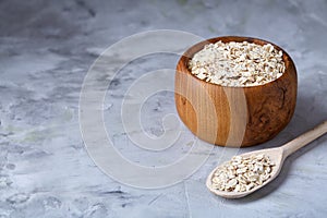 Oat flakes in bowl and wooden spoon on wooden background, close-up, top view, selective focus.