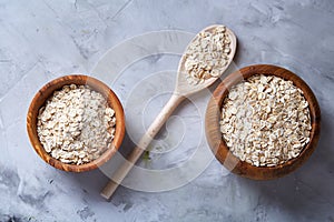 Oat flakes in bowl and wooden spoon on wooden background, close-up, top view, selective focus.