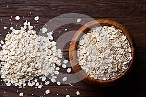 Oat flakes in bowl and wooden spoon on wooden background, close-up, top view, selective focus.