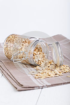 The oat flakes in glass jar on brown towel.
