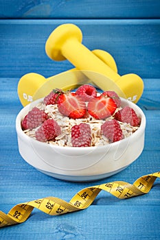 Oat flakes or oatmeal with fruits, tape measure and dumbbells, healthy, sporty lifestyle and nutrition concept