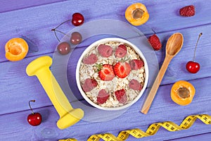 Oat flakes or oatmeal with ripe fruits, tape measure and dumbbells, healthy, sporty lifestyle and nutrition concept