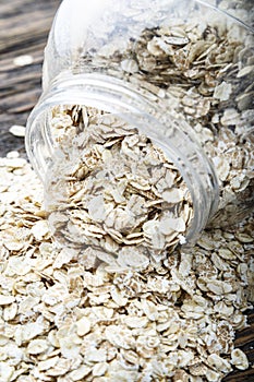 Oat flakes spilling out of glass jar on wooden background
