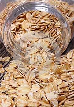 Oat flakes spilling out of jar on wooden background