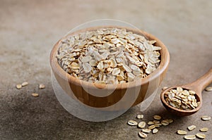 Oat flakes in a wooden bowl and wooden spoon on light brown background.
