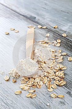 Oat flour in wooden spoon with oatmeal flakes