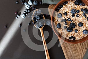 Oat granola with fresh blueberries and currants in a clay bowl over dark grunge surface. Top view, copy space. Wooden background.