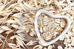Oat groat in heart shaped bowl, oatmeal grain for healthy diet on oat ears plants background photo