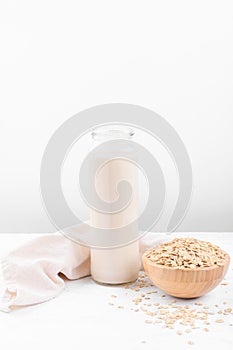 Oat milk in a bottle and a bowl with oat flake on white table