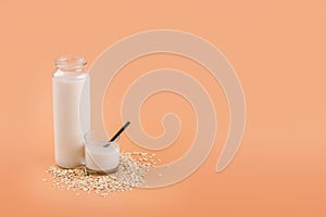 Oat milk in bottle and glass on the oat flake on pastel peach color background