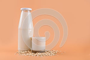 Oat milk in bottle and glass on the oat flake on pastel peach color background