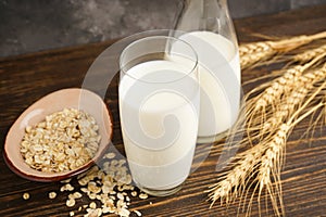 Oat milk in the glass with jug of milk and oat on a wooden background