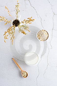 Oat milk in a glass, oatmeal in a bowl and ears in a jug on a light table. Alternative plant food. Vertical view