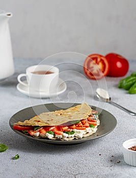Oat pancake stuffed with curd cheese, tomato and basil on a gray plate