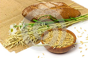 Oat seeds in wooden bowl, oat ears and homemade bread on sackcloth isolated on white background