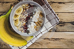 Oatmeal with bananas, cranberry, chia seeds, coconut shreds, almonds. Healthy breakfast concept. Rustic wooden background.