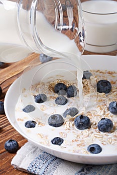 Oatmeal with blueberries and milk is poured from a jug