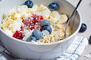 Oatmeal bowl with banana, berries, hemp seeds and coconut slices. Healthy vegan breakfast concept