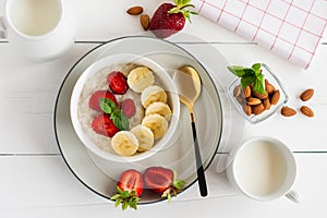 Oatmeal bowl with banana and strawberry, milk glass on a white table. healthy organic food