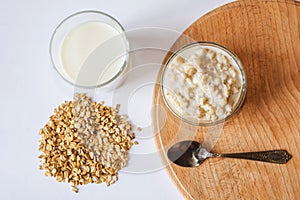 Oatmeal in a bowl with a glass of milk, a spoon and oatmeal on a wooden board. A healthy and nutritious morning breakfast