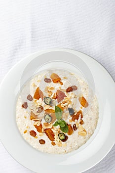 Oatmeal breakfast with raisins, dried apricots and peanuts on white background