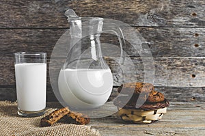 Oatmeal chocolate chip cookies, jug and glass of milk, rustic wooden background.