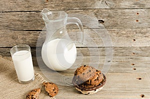 Oatmeal chocolate chip cookies, jug and glass of milk, rustic wooden background.