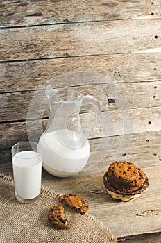 Oatmeal chocolate chip cookies, jug and glass of milk, rustic wooden background.