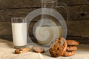 Oatmeal chocolate chip cookies, jug and glass of milk, rustic wooden background.