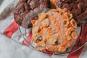 Oatmeal cookie milk cookie and chocolate chip nut cookie on grate metal red and white napkin black background.