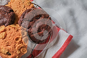 Oatmeal cookie milk cookie and chocolate chip nut cookie on grate metal red and white napkin black background.