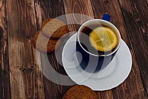 Oatmeal cookies with chocolate chips on a white saucer. A cup of black tea on a wooden background