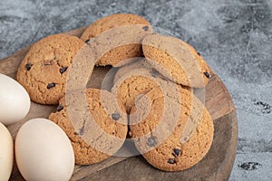 Oatmeal cookies with chocolate drops on a wooden board with eggs around