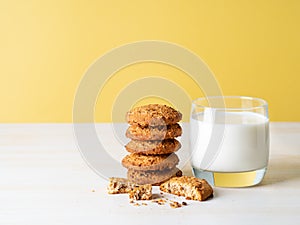 Oatmeal cookies with flax seeds and milk in a glass, healthy snack. Light background, bright yellow wall