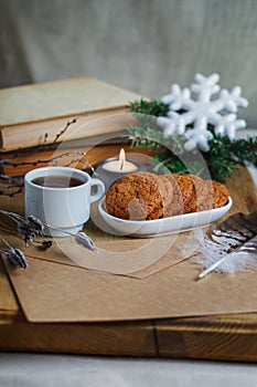 Oatmeal cookies with hot tea on a natural wood kitchen board. Winter composition for the interior with snow-covered