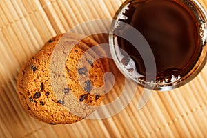 Oatmeal cookies with pieces of chocolate and a mug of coffee on a bamboo stand. Close-up