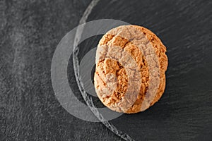 Oatmeal cookies three pieces stacked, on slate stone plate round, dark background, top view, selective focus