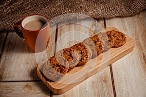 Oatmeal cookies on a wooden plate with a cup of coffee with milk. The concept of natural and delicious food.