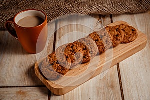 Oatmeal cookies on a wooden plate with a cup of coffee with milk. The concept of natural and delicious food.
