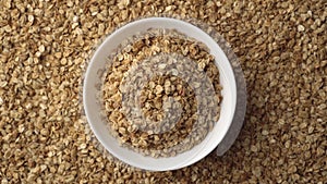Oatmeal or crunchies in a white bowl and with flakes in the background are slowly rotating. Concept of healthy food -